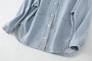 Detail of light blue denim shirt showing metal buttons and curved hem design