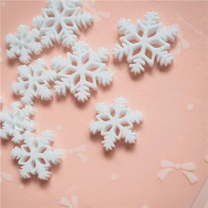 Sparkly white resin snowflake charms for DIY Christmas crafts on pink background