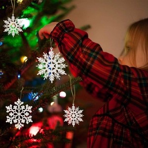 Girl hanging white glitter snowflake ornaments with gold strings on a Christmas tree