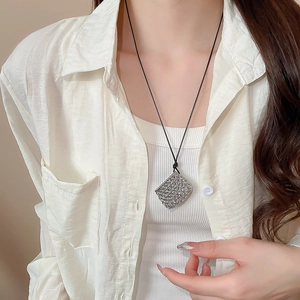 Close-up of a silver textured square pendant on a black cord necklace worn by a model