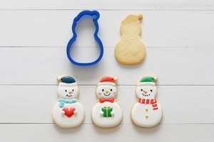 Detailed blue plastic snowman cookie cutter with finished sugar cookies on white wood