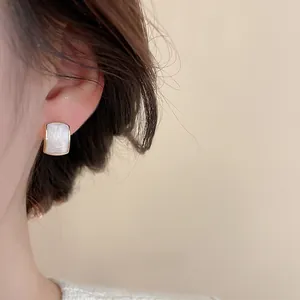 Close-up of elegant gold square earrings with white pearl inlay worn by a model