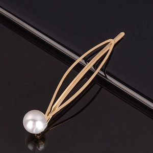 Barrette élégante en métal doré avec une perle unique sur une surface réfléchissante