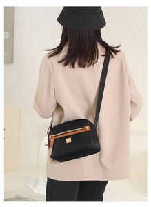 Rear view of model wearing black nylon crossbody bag with brown leather trim and metal logo