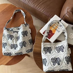 Off-white canvas shoulder bag with black butterfly embroidery on a wooden table