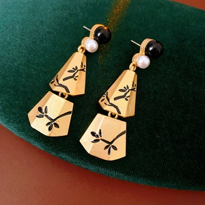 Detail of gold fringe earrings with black branch pattern and white pearl accents