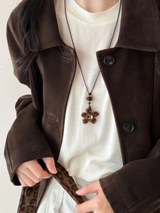 Close-up of leopard print flower pendant necklace worn by a model in brown suede jacket