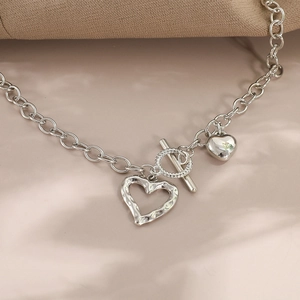 Detailed view of silver heart pendant necklace with vintage OT clasp on beige background