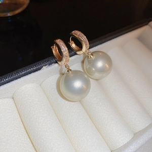 Macro shot of gold-plated earrings featuring crystal-encrusted hoops and round pearls