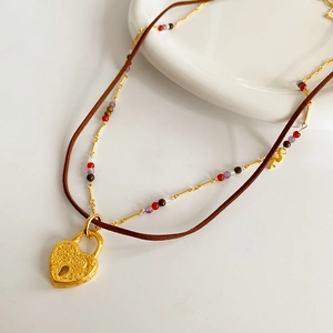 Detail of double-layer necklace with golden heart lock pendant and brown leather cord