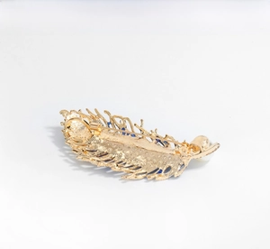 Detail view of gold peacock feather brooch with pin clasp, blue enamel, and white pearl