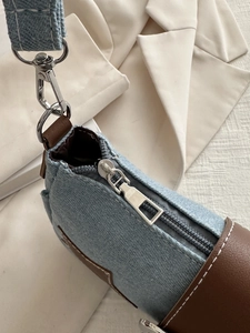 Detail of silver zipper and brown leather trim on light blue denim shoulder bag