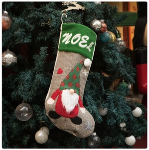 Detail of grey gnome Christmas stocking with NOEL embroidery hanging on a festive tree