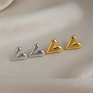 Close-up of polished 18K gold and silver heart stud earrings on silk fabric background
