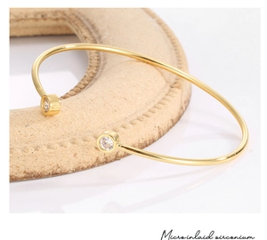 Macro detail of gold-plated open bangle featuring micro-inlaid round cubic zirconia stones