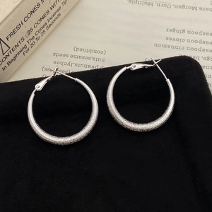 Macro detail of large silver frosted earrings with sparkling texture on black velvet background