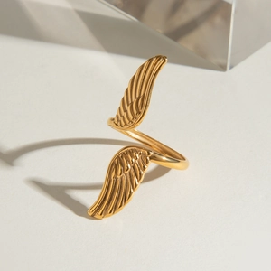 Golden stainless steel angel wing ring featuring a polished finish on a minimalist surface