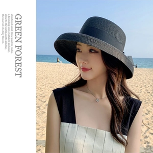 Detailed view of a wide-brimmed black straw hat with elegant ribbon on a sunny beach