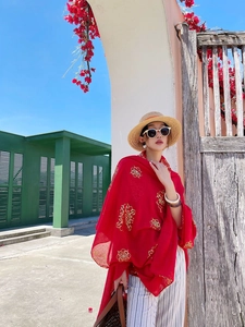 Detail of red beach scarf with golden vintage patterns and stylish straw hat accessory