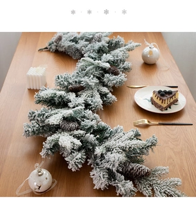 Close-up of snowy Christmas garland with pine cones on a rustic wooden dining table