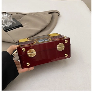 Close-up of retro radio-shaped crossbody bag with glossy burgundy finish and gold hardware