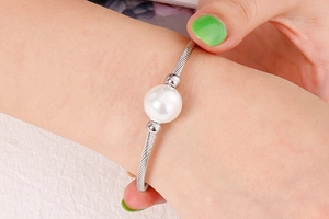 Détail du bracelet en acier inoxydable torsadé avec une grande perle blanche sur main