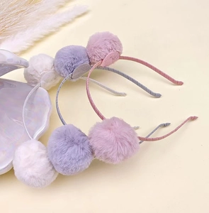 Detailed view of pink, grey, and white plush pom-pom headbands for kids' hair styling