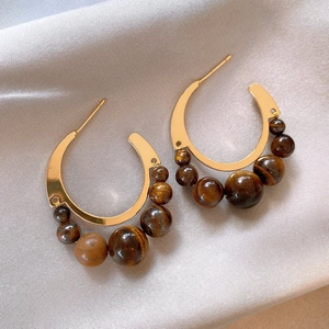 Close-up of golden C-shaped hoop earrings with tiger eye beads on champagne silk fabric