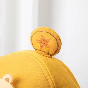 Détail de la décoration d'oreille d'ours et broderie d'étoile sur casquette bébé jaune