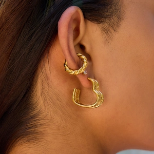 Close-up of a model wearing golden twisted hoop and hollow heart earrings in stainless steel