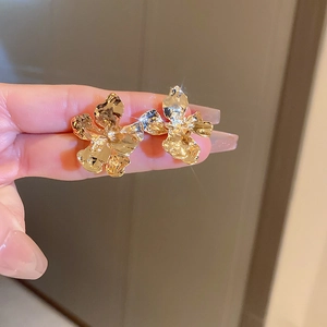 Golden metallic flower earrings with irregular hammered texture shown in hand