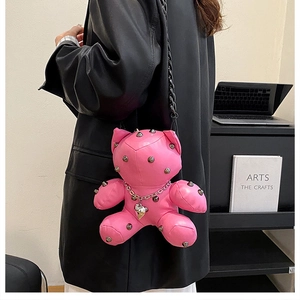 Pink leather teddy bear crossbody bag with silver studs worn by a model in a studio setting