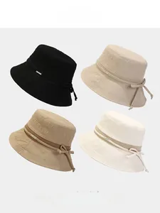 Détail de quatre chapeaux de soleil en beige et noir avec logo Lucky et nœuds décoratifs