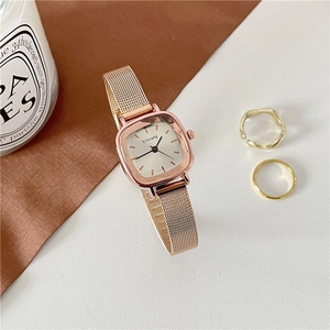 Close-up of rose gold square watch with white dial and metal mesh strap on table