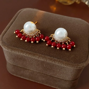 Close-up of gold-plated tassel earrings with white pearls and red beads on brown velvet