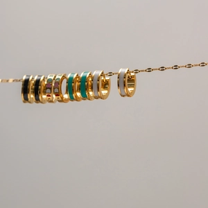 Detailed view of colorful enamel huggie earrings on a gold chain in various stylish colors