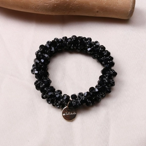 Detail of black faceted bead hair tie bracelet with a gold engraved logo tag on fabric