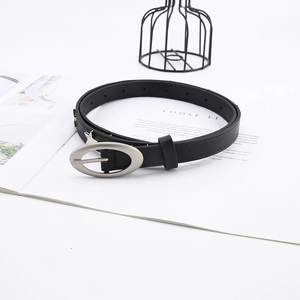 Detail of slim black leather belt for women featuring an oval silver buckle on a white book