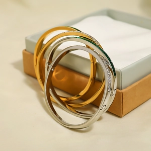 Detailed view of three stackable gold and silver bracelets with green zircon by a gift box