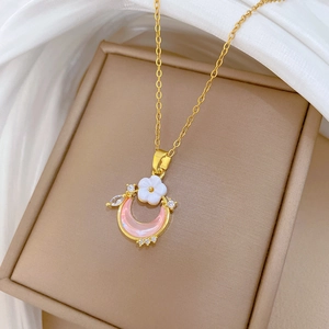 Detail of gold necklace with pink crescent moon pendant featuring a white flower and gems