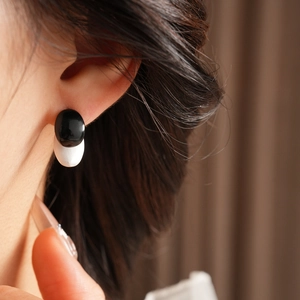 Close-up of minimalist black and white oval earrings worn by a model to show detail