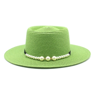 Dettaglio di un cappello di paglia verde chiaro con decorazione di perle e finitura oro