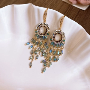 Detail of gold tassel earrings with grey-blue crystal beads in a shell ceramic dish