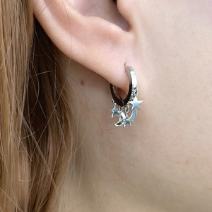 Detailed view of sterling silver star and moon hoop earrings worn on earlobe