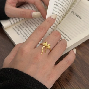 Detail of a golden bow ring worn on finger against an aesthetic book and wooden background
