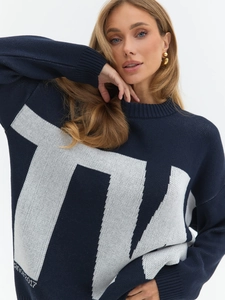 Detail of navy knit sweater showing white geometric letter jacquard and ribbed cuffs