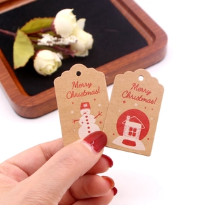 Hand holding two Kraft paper Christmas gift tags with red snowman and house patterns