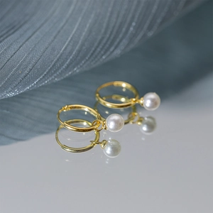 Macro shot of elegant gold pearl earrings reflecting on a clean mirror surface