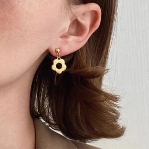 Elegant gold-tone hollow flower drop earrings worn by a model in a minimalist style