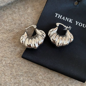Macro shot of silver shell-shaped croissant hoop earrings on a black display card